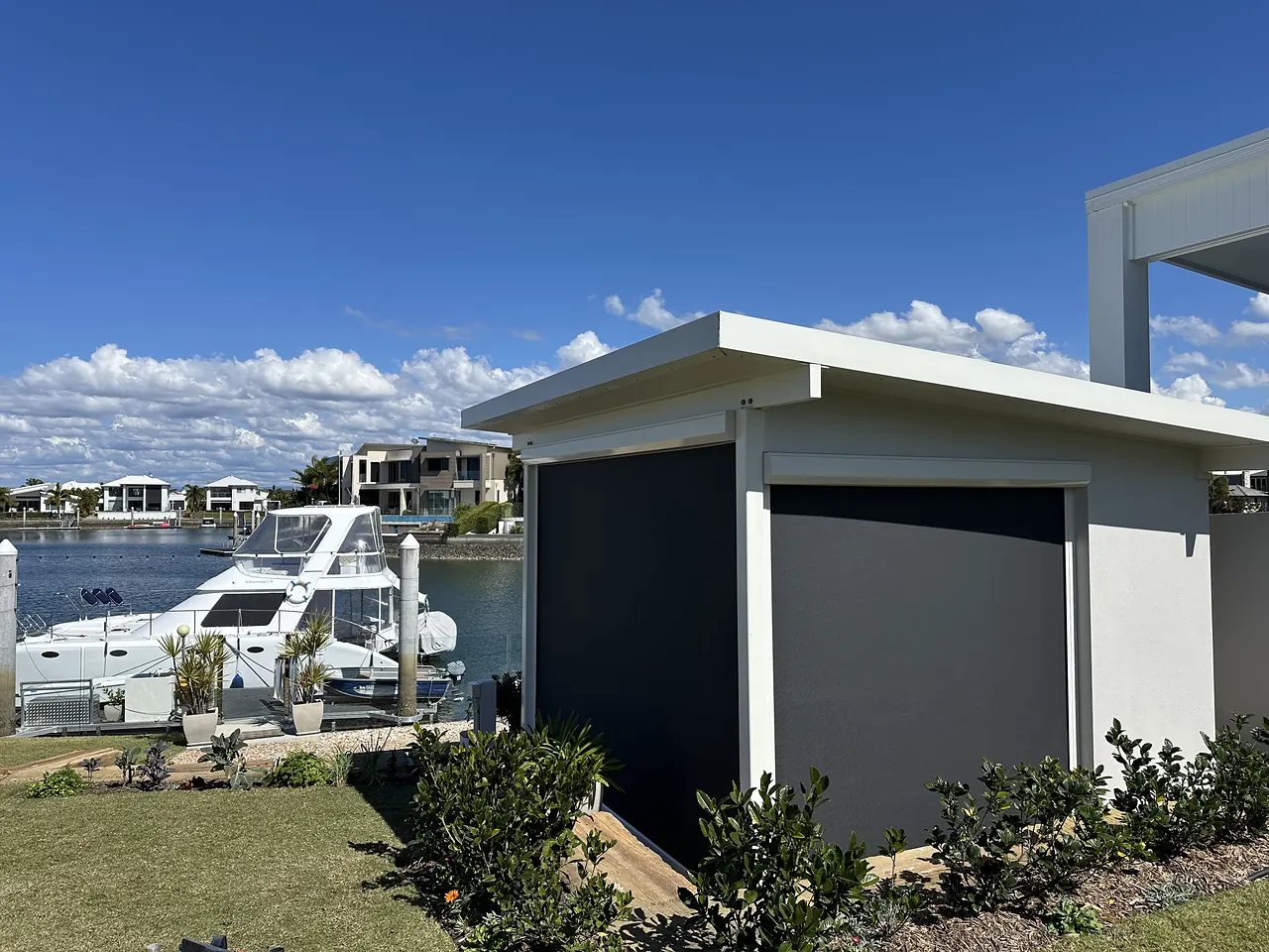 Charcoal zip track blinds lowered on a white canal-side pavilion, with a boat moored behind