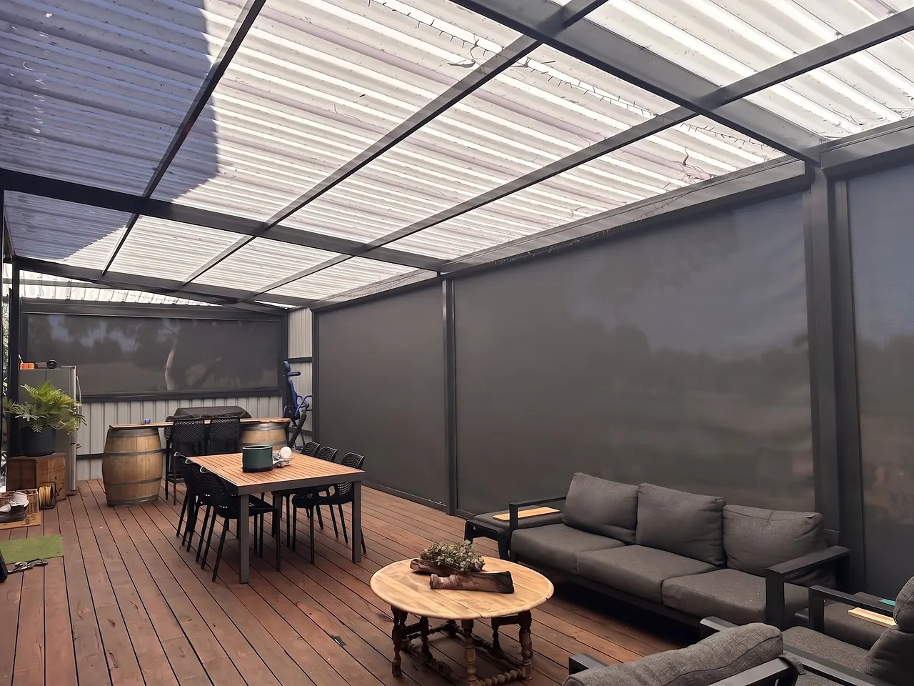 Timber deck and outdoor lounge enclosed by charcoal zip blinds under a pergola