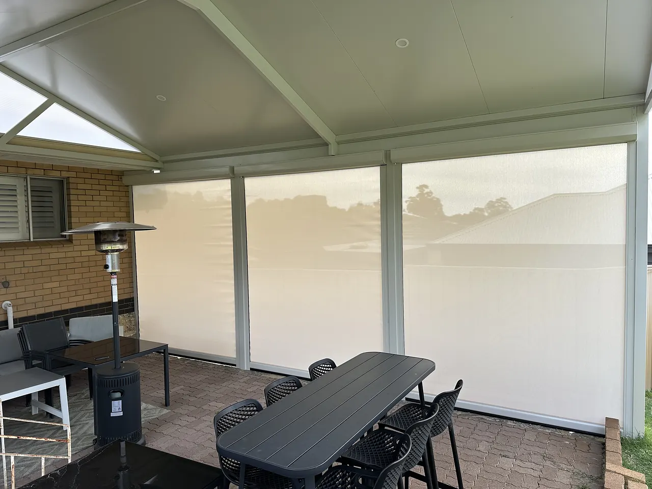 Light-coloured zip blinds lowered around a patio dining setting