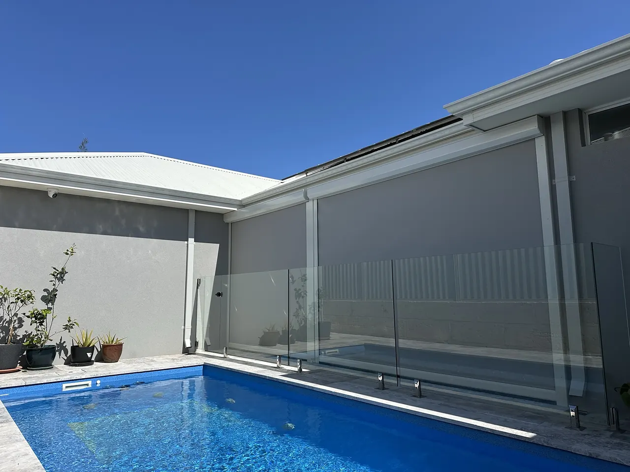 Grey zip blinds beside a swimming pool and glass pool fence