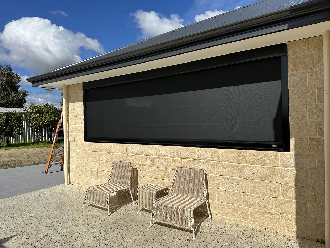 Charcoal zip blind across a wide alfresco opening, with sun loungers on the paving
