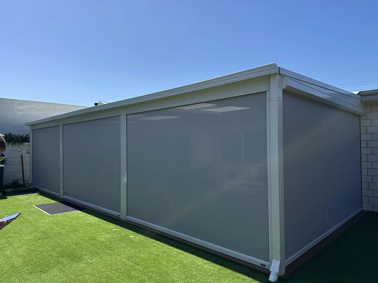 Grey zip blinds wrapping a large patio beside an artificial lawn