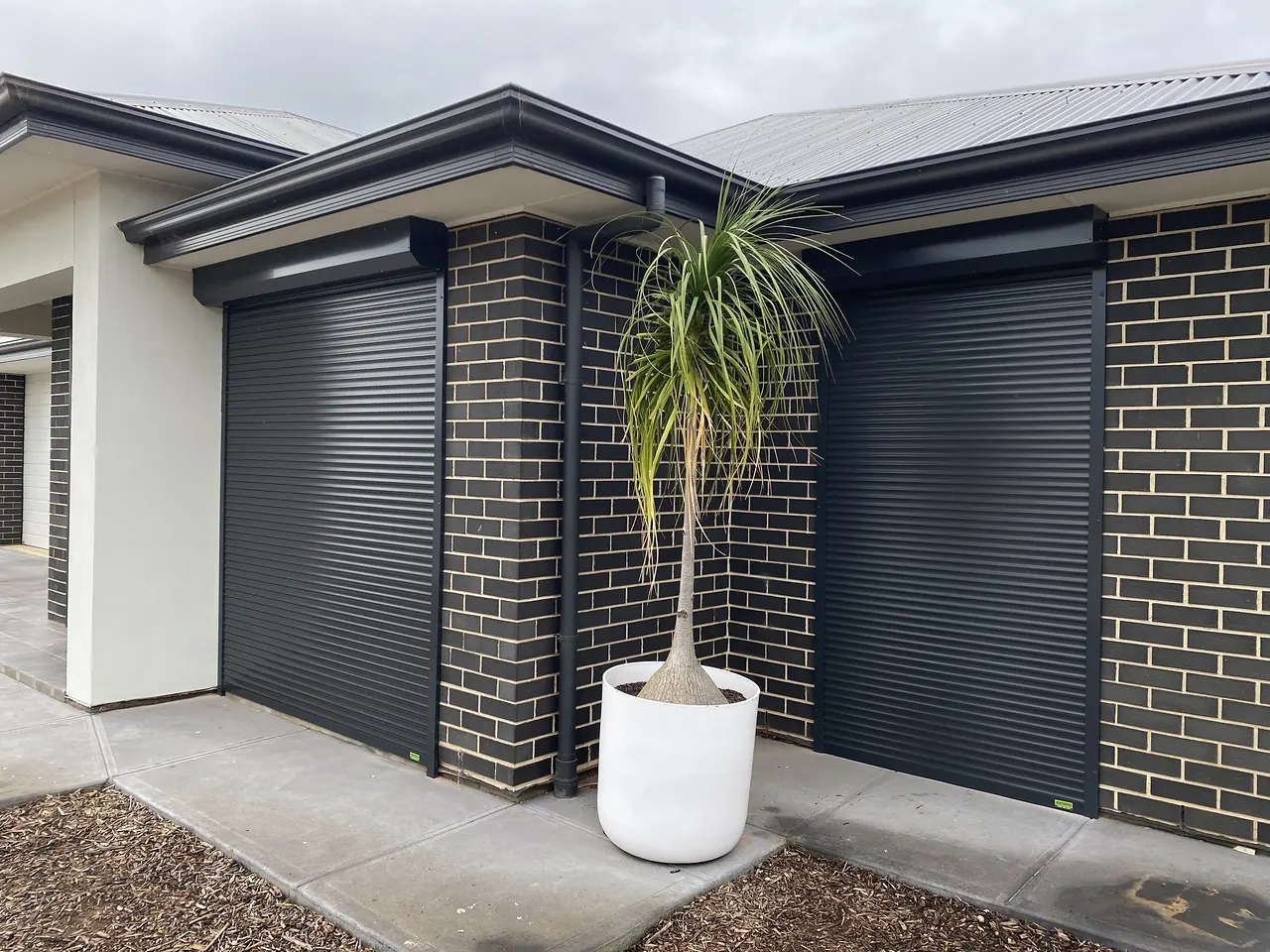 Charcoal roller shutters on two windows of a dark brick home