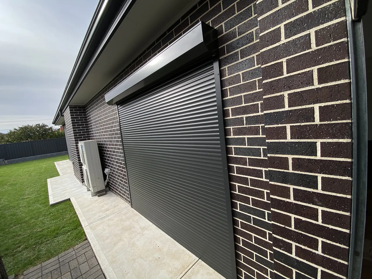 Charcoal roller shutter on the side of a dark brick home
