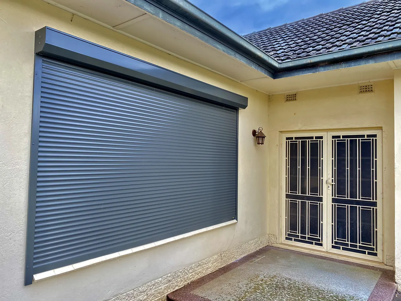 Charcoal roller shutter on a large front window beside a security door