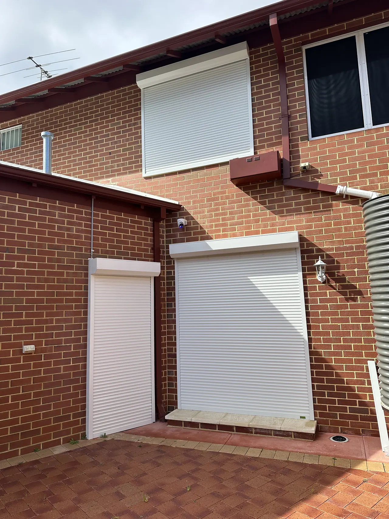 White roller shutters on the windows and back door of a two-storey brick home