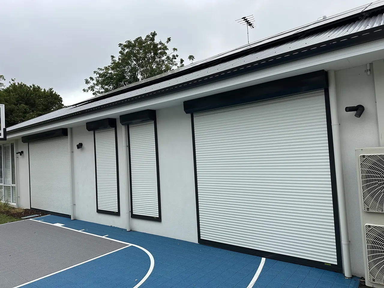 White roller shutters on a modern home beside a backyard sports court